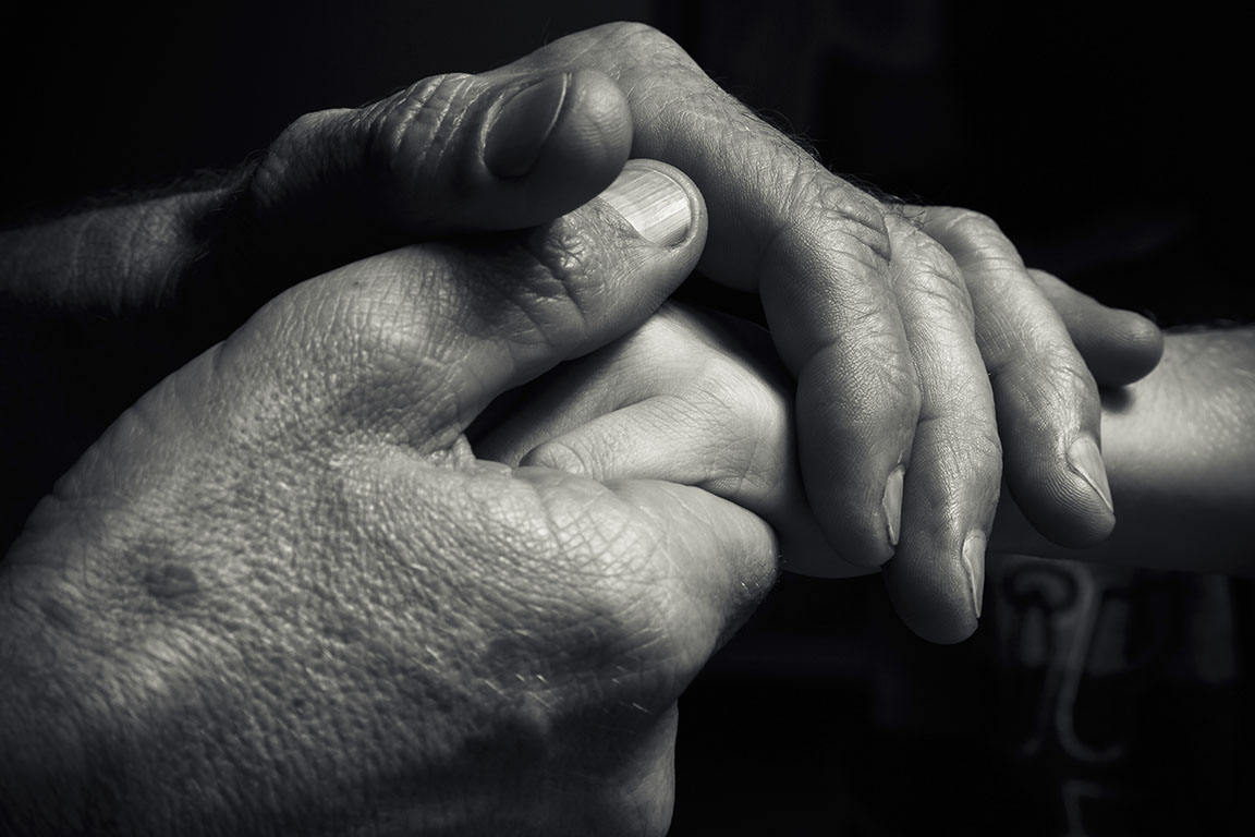 Mãos de um homem idoso, segurando a mão de um homem mais jovem. Muita textura e caráter nas mãos do velho. Preto e branco