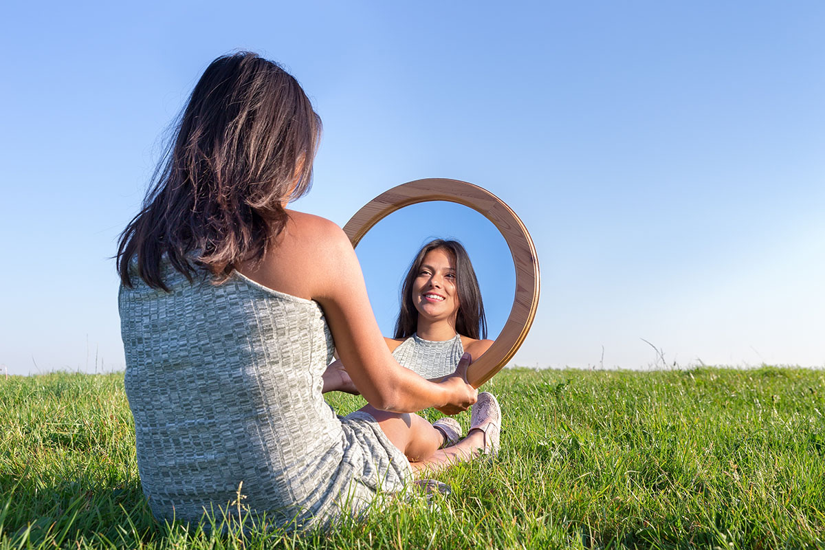 Mulher sentada na grama olhando para sua imagem no espelho