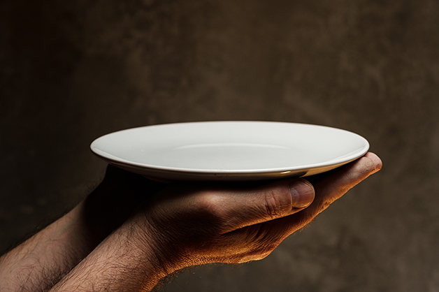 Masculinas mãos segurando um prato vazio em fundo escuro, falta de comida, fome e conceito de crise